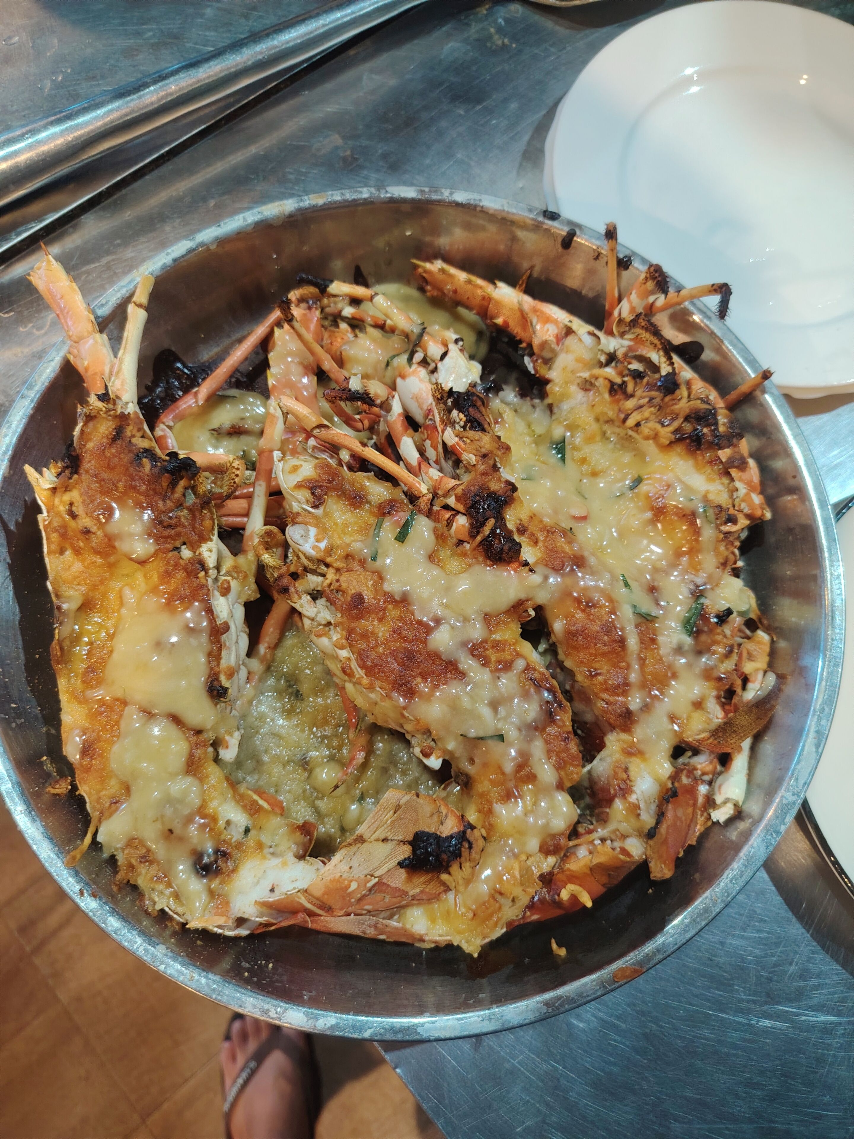 A metal bowl containing a dish with fried seafood and melted cheese.