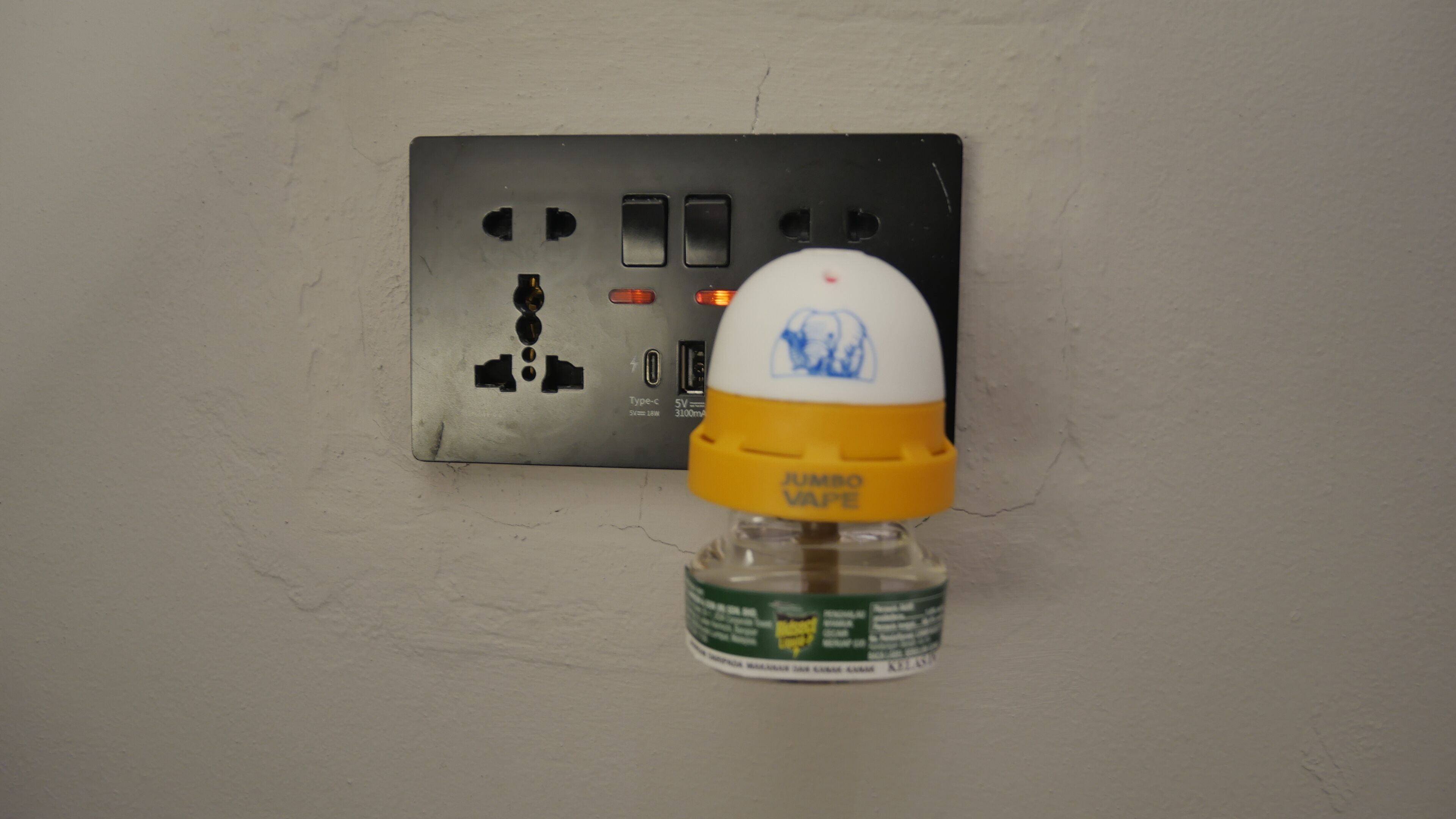 A power outlet with a plug and a safety cap on the wall.