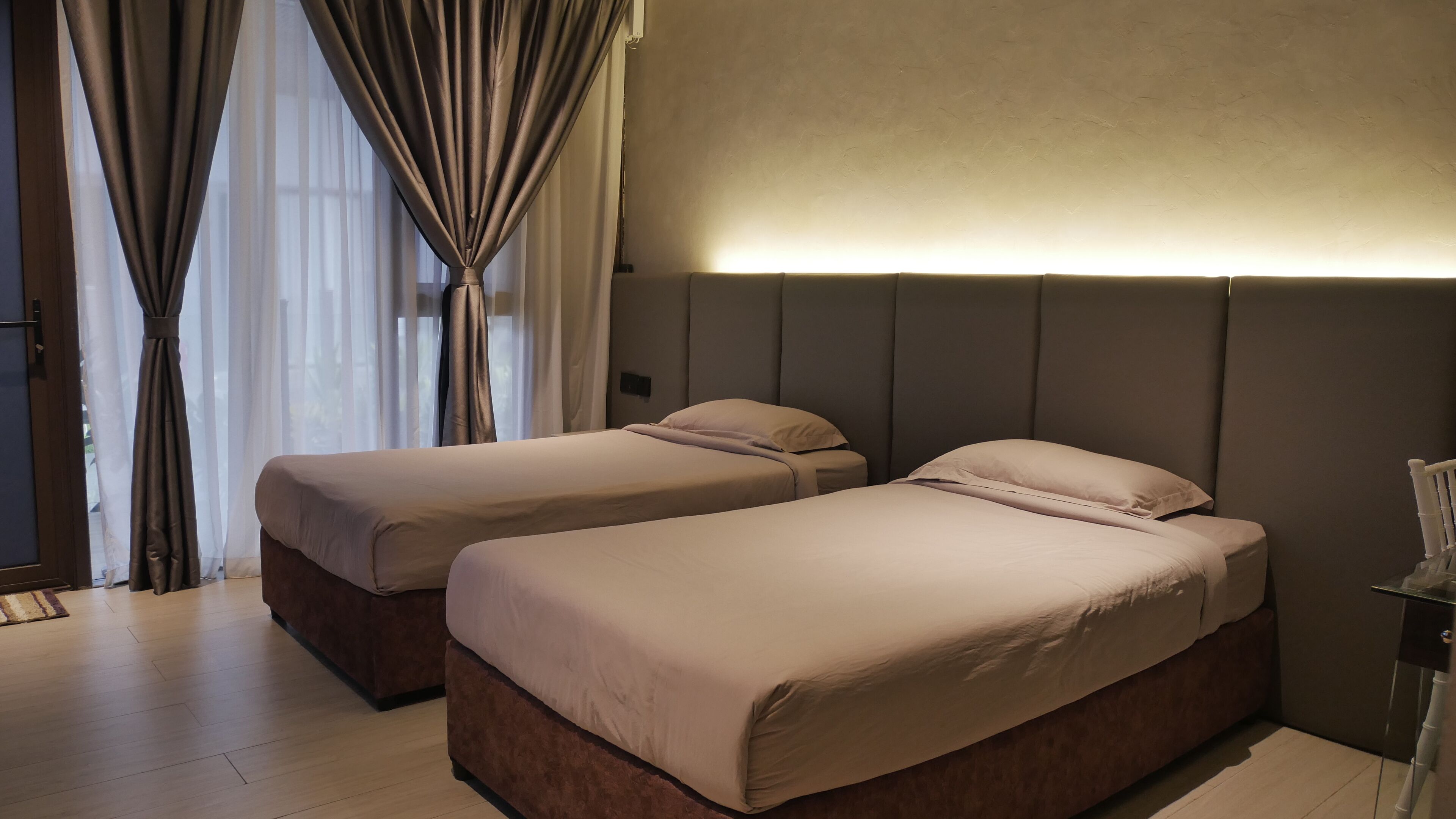 A hotel room with two beds, a large window with curtains, and a modern headboard.