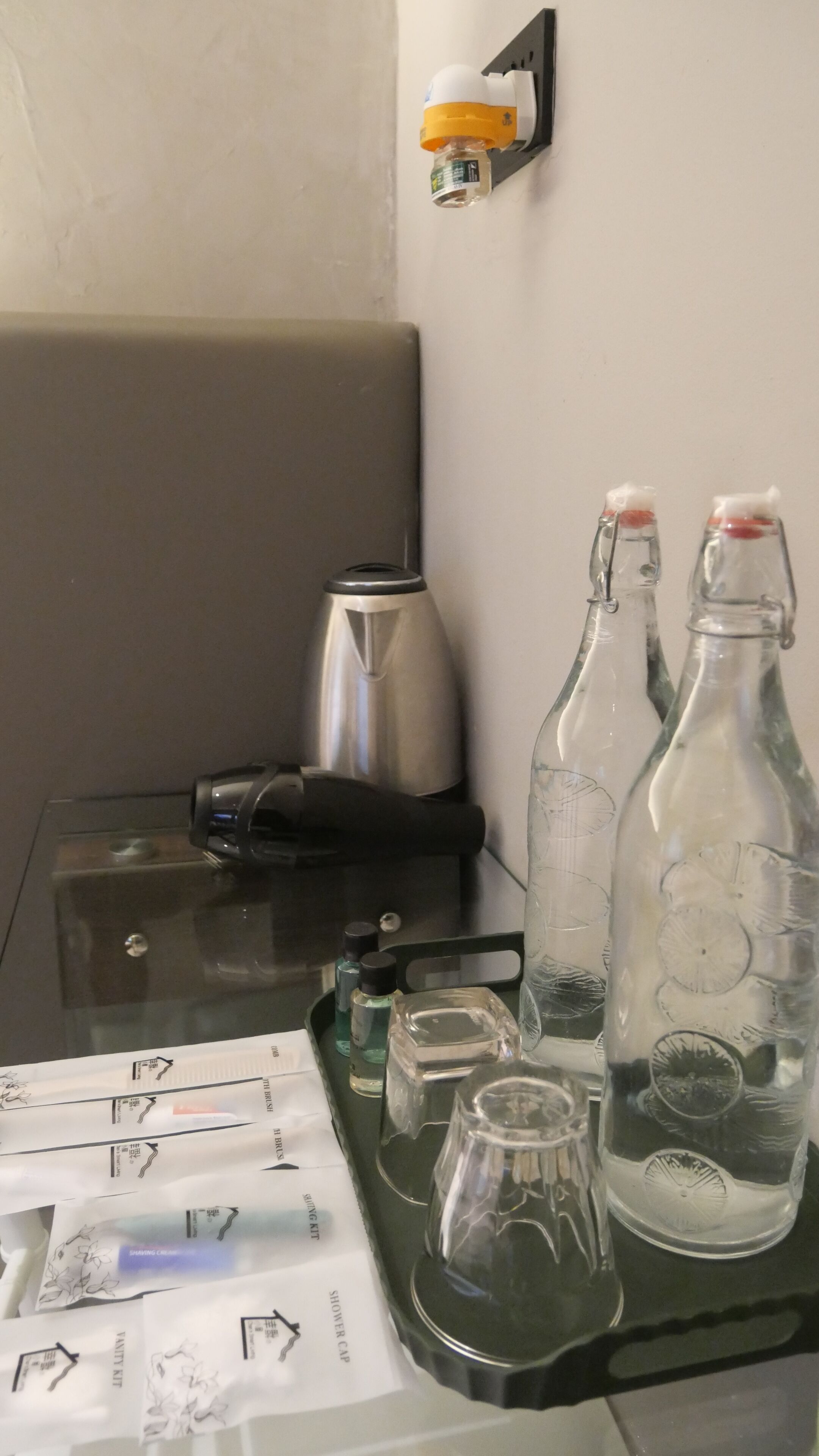 A glass table with a kettle, two bottles, a small glass, and a tray with papers.