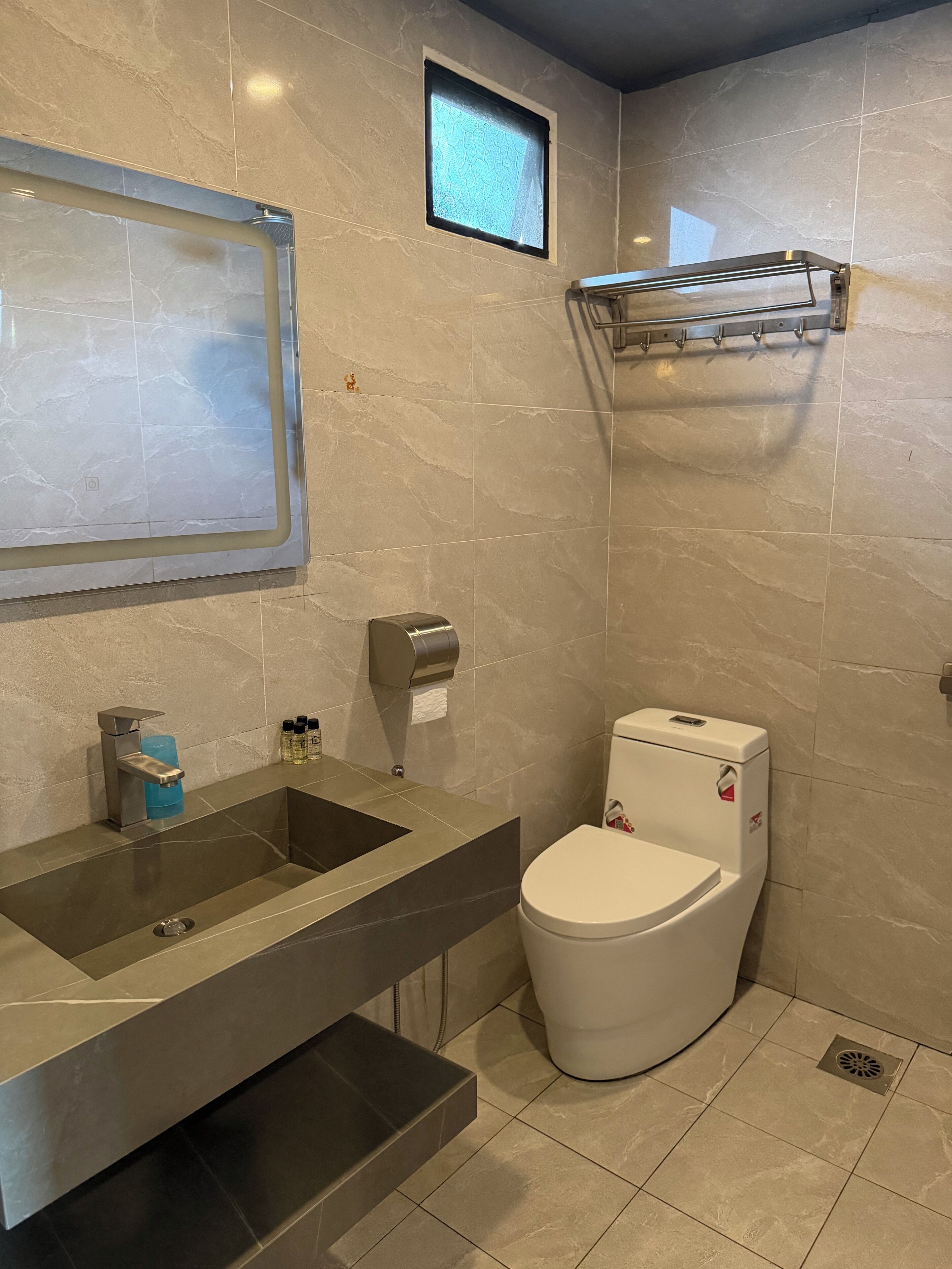 A modern bathroom with a large mirror, a sink, a toilet, and a small window.