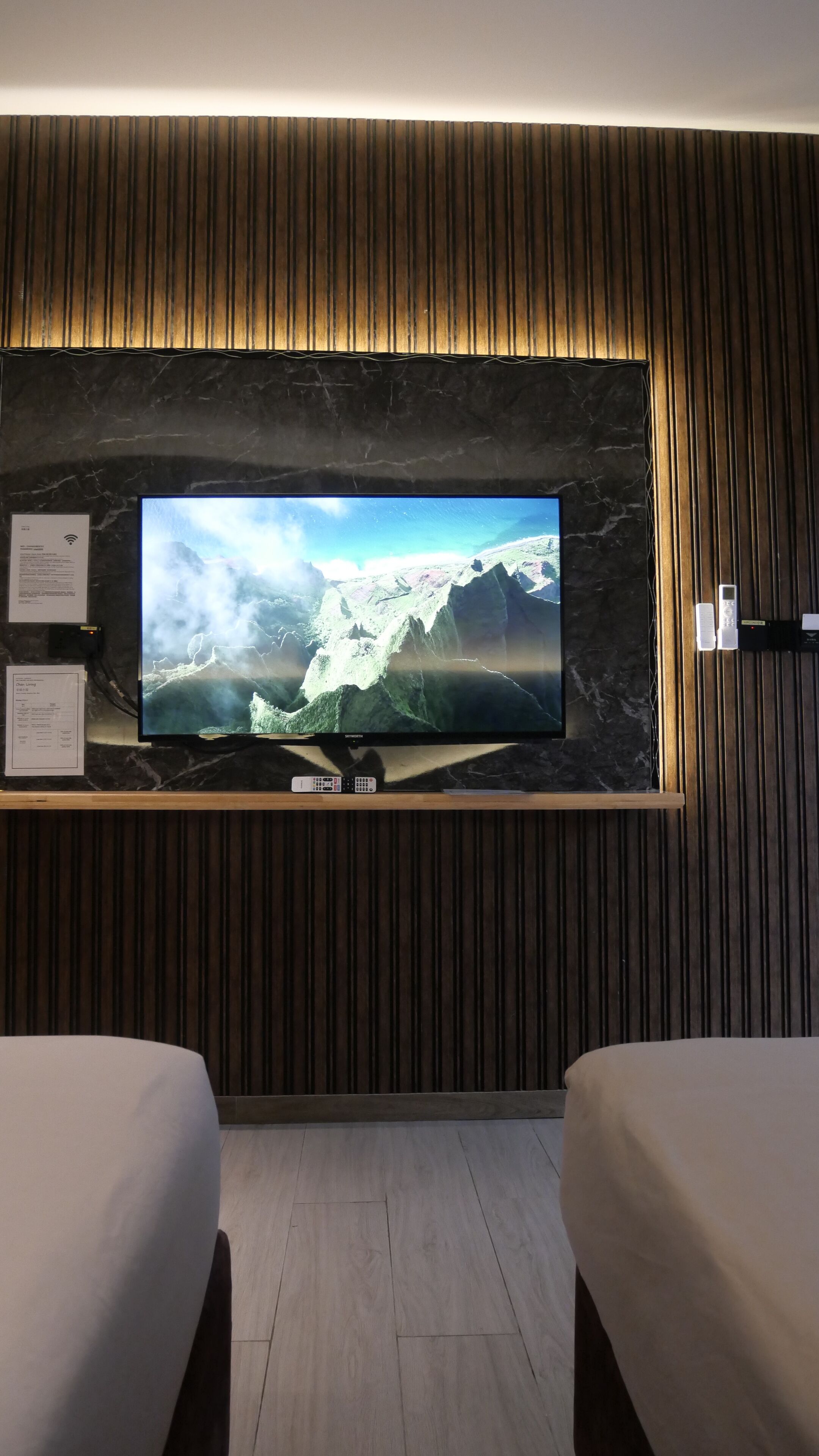 Ein Hotelzimmer mit einem großen Flachbildfernseher an einer Marmorwand, zwei Betten und einer Holzpaneelausstattung.