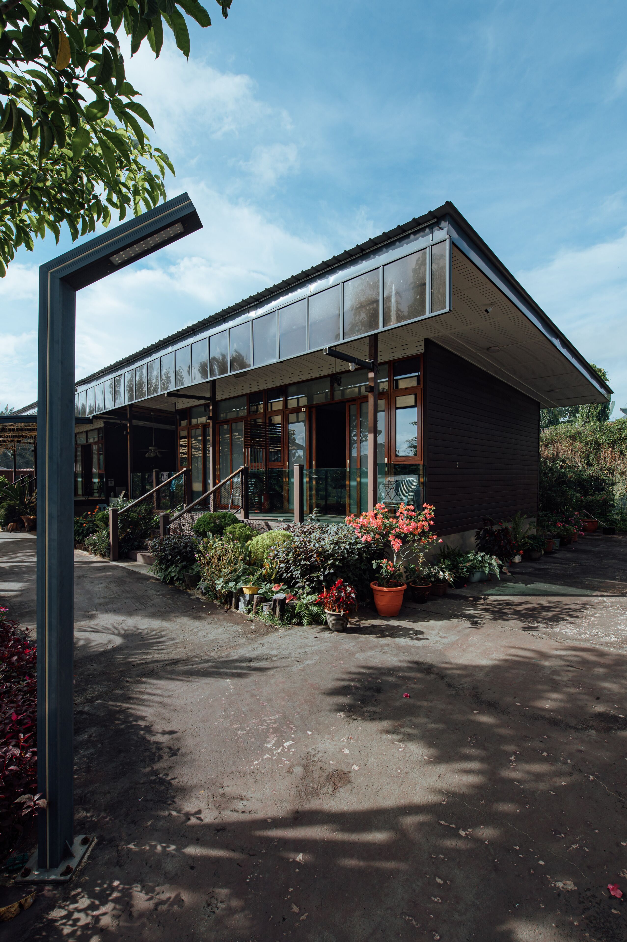 A modern building with large windows, a covered entrance, and a garden with various plants and flowers.