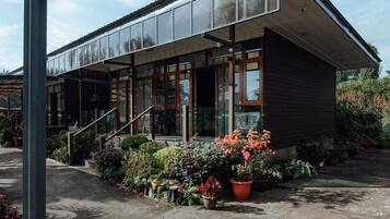 A modern building with large windows, a covered entrance, and a garden with various plants and flowers.
