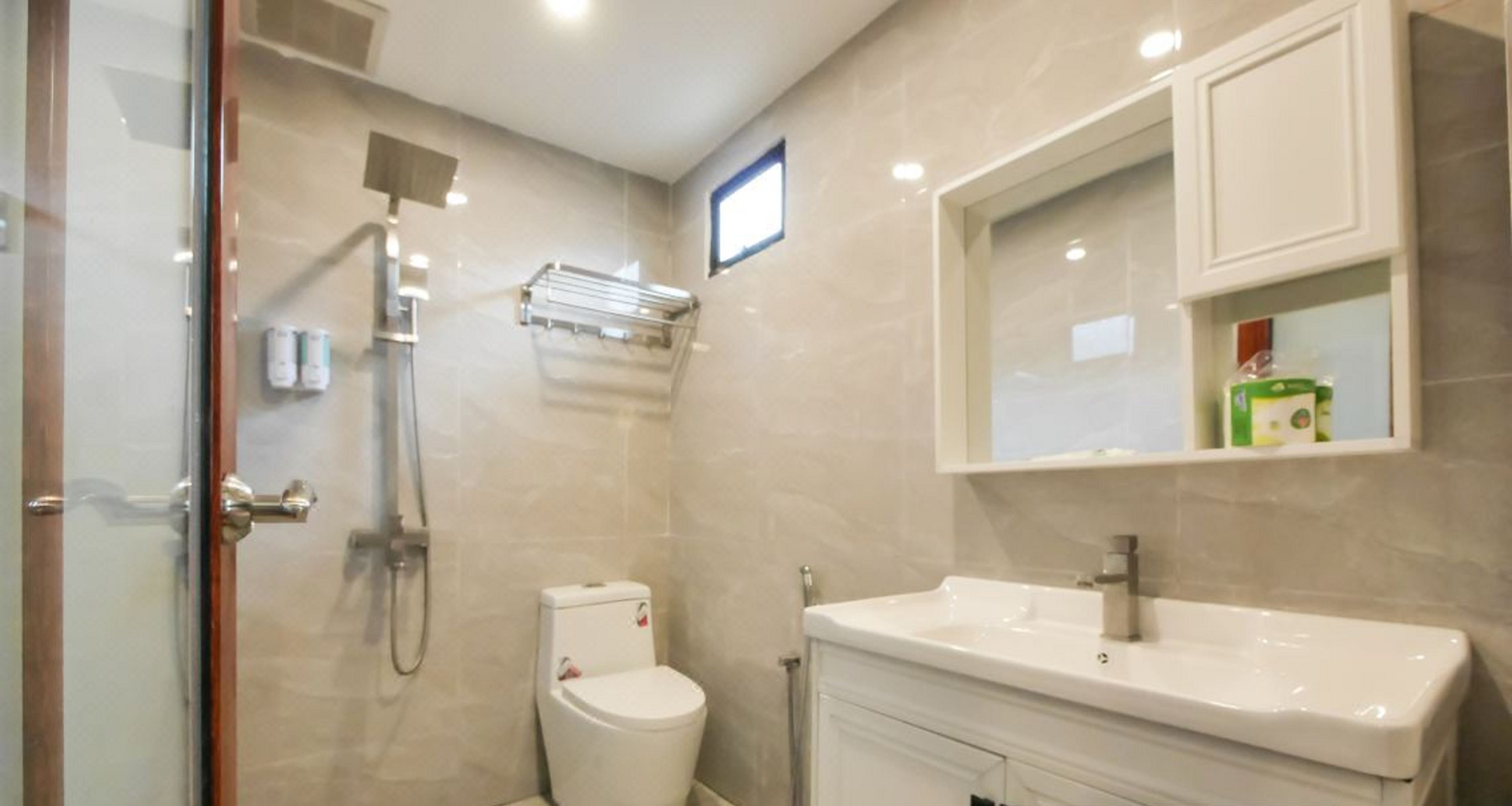 Une salle de bain moderne avec une douche à parois de verre, des toilettes blanches et un meuble-lavabo surmonté d’un miroir.