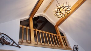 A wooden balcony with a railing, a chandelier, and a wall-mounted decorative item. - Lakefront Retreat on Lake Flower near Lake Placid (Saranac Lake)