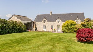 A stone building with a sloped roof, a well-maintained lawn, and various shrubs.