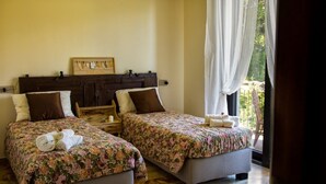 A room with two beds, each with floral bedding and pillows, a wooden headboard, and a window with sheer curtains.