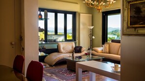 A living room with a sofa, a glass coffee table, and a view of mountains through large windows.