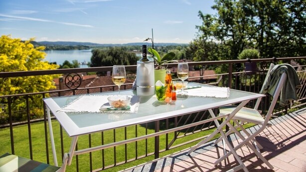 A glass table with a view of a lake, surrounded by greenery and a clear sky.