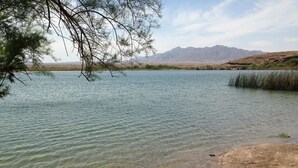 A calm lake with clear water, surrounded by a natural landscape and mountains in the background.