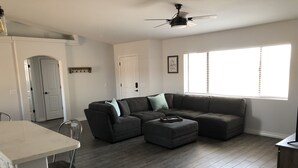 A modern living room with a sectional sofa, a dining table, and a ceiling fan.