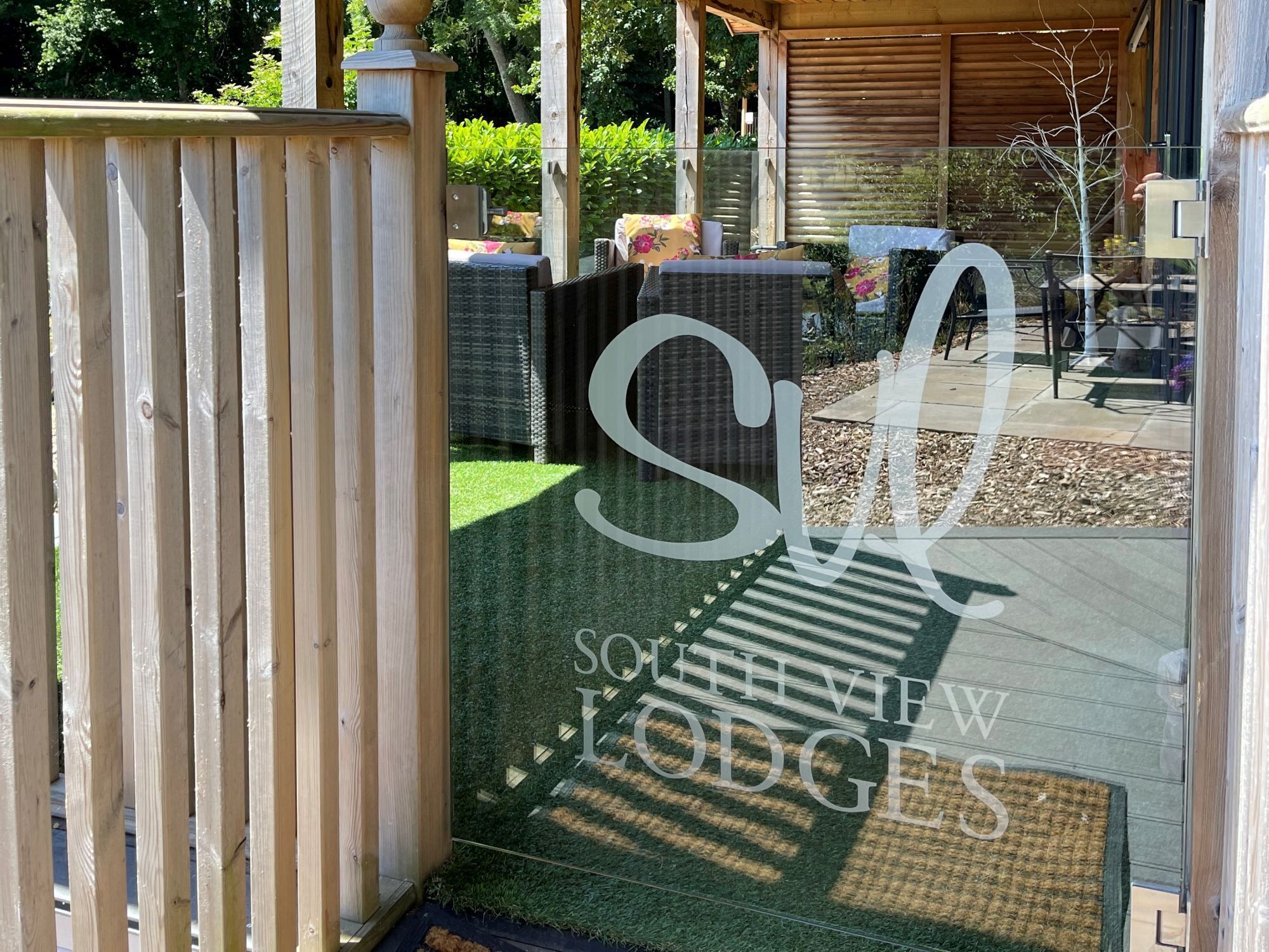 Um portão de madeira dá acesso a um pátio com mobiliário exterior e uma placa com a inscrição 'SOUTHVIEW LODGES'.