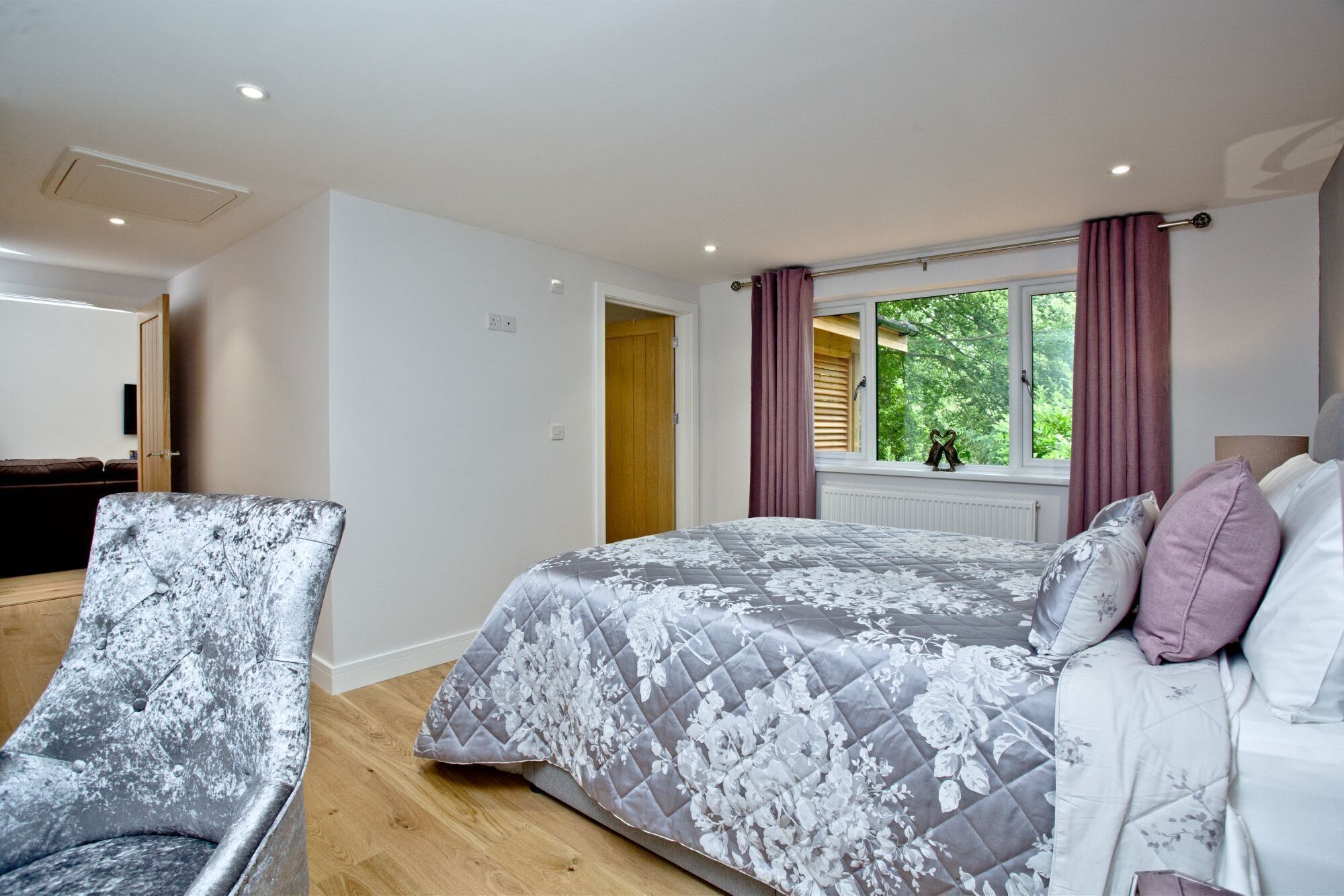 Une chambre à coucher avec un lit, une chaise, une fenêtre avec des rideaux et une vue sur la verdure à l’extérieur.
