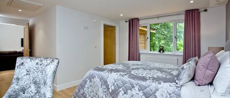 Une chambre à coucher avec un lit, une chaise, une fenêtre avec des rideaux et une vue sur la verdure à l’extérieur.