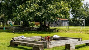Un espacio con césped, una banca de madera, una mesa de picnic y un pequeño hogar para fuego.