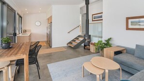 A modern living room with a wooden dining table, a sofa, and a small coffee table. There is a staircase leading to an upper level and a fireplace. - FortyTwo Mini |Gracetown (Gracetown)