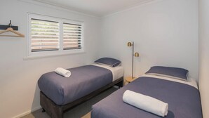 A room with two beds, each with a pillow and a rolled towel. There is a window with blinds, a floor lamp, and a small table. - FortyTwo Mini |Gracetown (Gracetown)