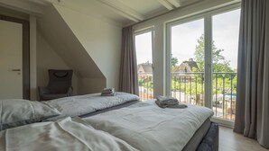 Un dormitorio con una cama grande, una silla y vistas a un balcón con casas.