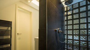 Un baño moderno con una pared de azulejos oscuros, una cabina de ducha de vidrio y una puerta a la vista.