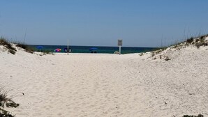 Una playa arenosa con cielo despejado. Se ven tres sombrillas y un cartel.