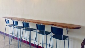 Uma área de bar com um balcão de madeira comprido e quatro cadeiras azuis.