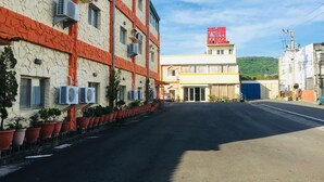 Um edifício com várias unidades de ar condicionado, fachada vermelha e branca, e área de estacionamento com vasos de plantas.