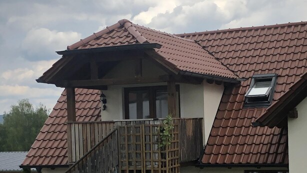 Een huis met twee verdiepingen, voorzien van een dak met rode tegels, een houten trap en een klein balkon.