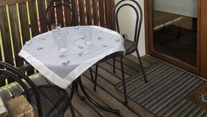 Een overdekt terras buiten, met een tafel en stoelen, een houten balustrade en een uitzicht op huizen op de achtergrond.