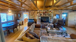 A log cabin interior with a stone fireplace, wooden beams, a dining area, and a cozy seating area.