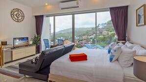 A modern hotel room with a large bed, a TV, a desk, and a view of a cityscape. - Chic Condo Karon by RESAVA (Karon)