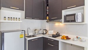 A compact kitchen with dark cabinets, a white countertop, a microwave, a kettle, and a sink. - Chic Condo Karon by RESAVA (Karon)