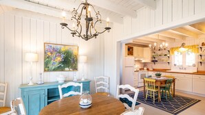 A dining area with a wooden table and white chairs, a blue cabinet, and a chandelier. - Sea Rose Cottage - Cozy, Comfortable, Ocean Views on Orr's Island, Harpswell, ME (Harpswell)