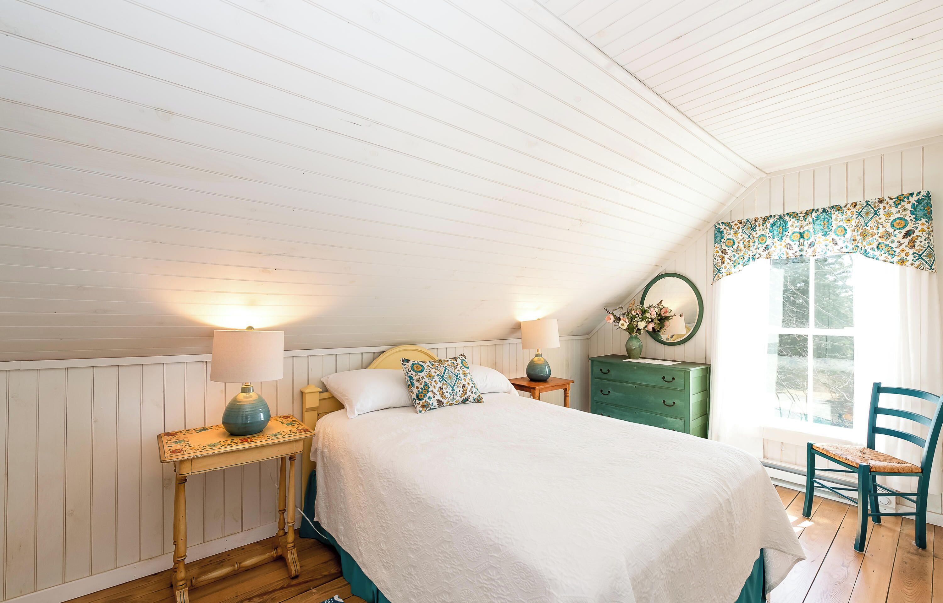 A bedroom with a bed, two bedside lamps, a dresser, a chair, and a window with curtains.