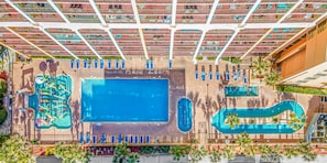 An aerial view of a hotel with a large central pool, multiple smaller pools, and a library with bookshelves.