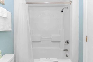 A white shower enclosure with a glass door, a handheld showerhead, a handheld faucet, and a toilet with a white seat.