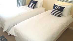 Duas camas de solteiro com roupa de cama branca e almofadas azuis-marinho com desenho de âncora.