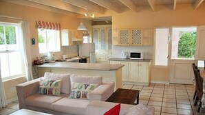 Uma sala de estar aconchegante com um sofá e uma mesa de centro, uma cozinha com armários brancos e um micro-ondas, e um espaço de jantar com uma cadeira.