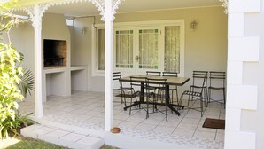 Um alpendre coberto com uma mesa e cadeiras de jantar, uma churrasqueira e vista para o jardim.