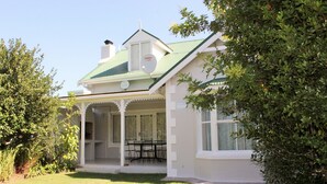 Uma casa branca com telhado verde, varanda coberta com mesa e cadeiras, e uma antena parabólica.