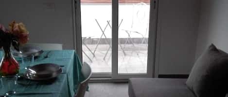 A room with a bed, a table set for two, and a sliding glass door leading to an outdoor area.