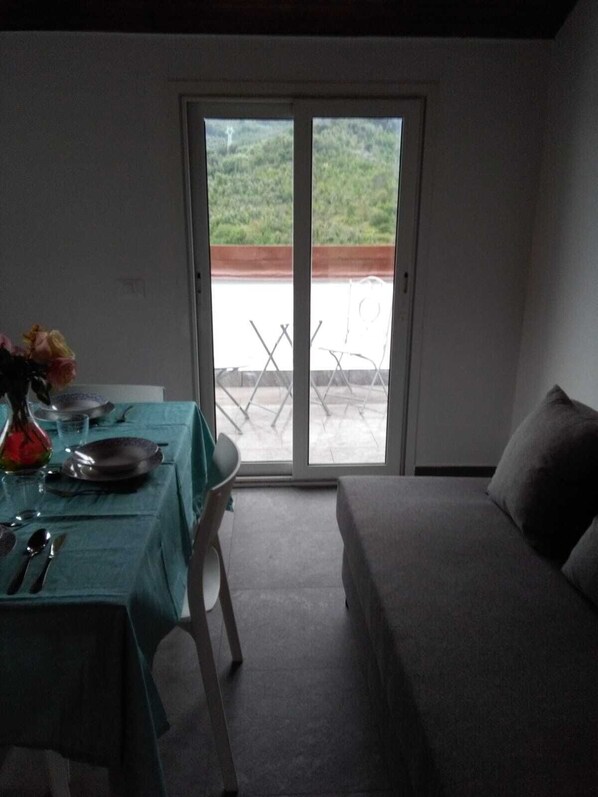 A room with a bed, a table set for two, and a sliding glass door leading to an outdoor area.