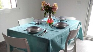 A dining table set with plates, glasses, and cutlery, covered by a teal tablecloth, with chairs around it.