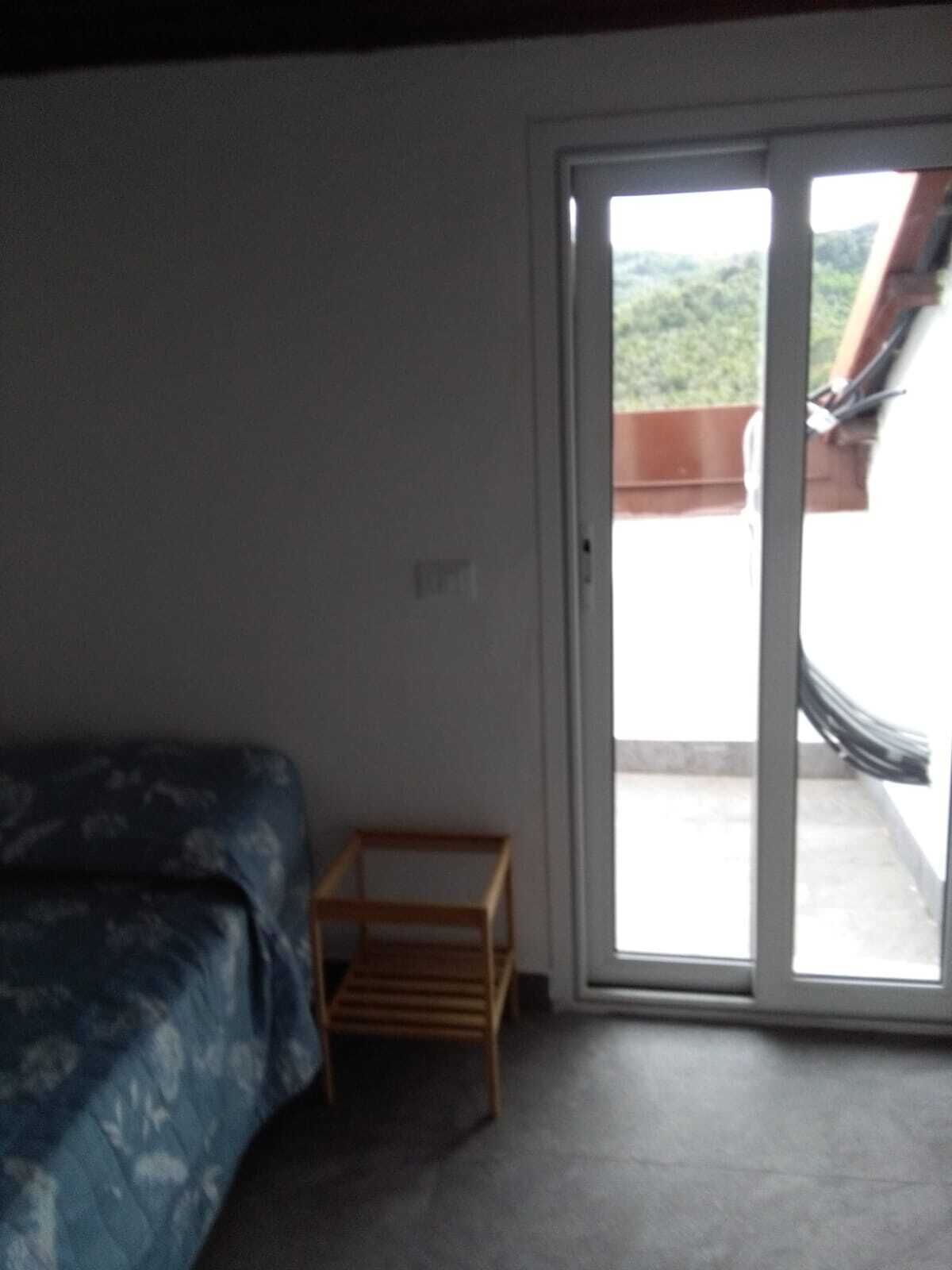 A room with a bed, a small wooden table, and a sliding glass door leading to an outdoor area.