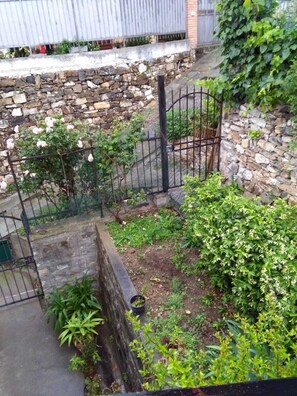 A stone wall with a metal fence, a garden with various plants, and a building in the background.