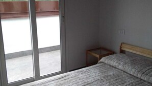 A bedroom with a bed, a wooden headboard, a small table, and a sliding glass door leading to a balcony.