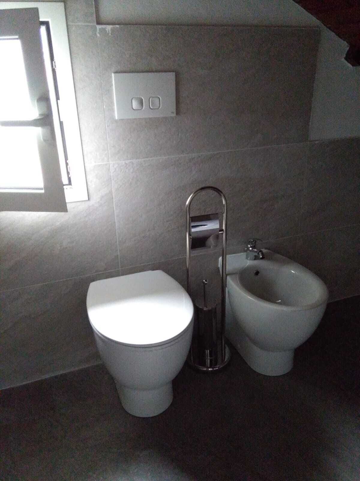 Een moderne badkamer met toilet, bidet en lichtschakelaar aan de muur.