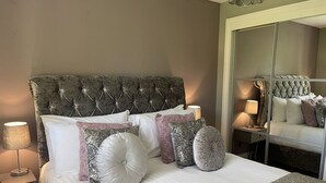 Un letto ben rifatto con una testiera imbottita, numerosi cuscini e una lampada da comodino.