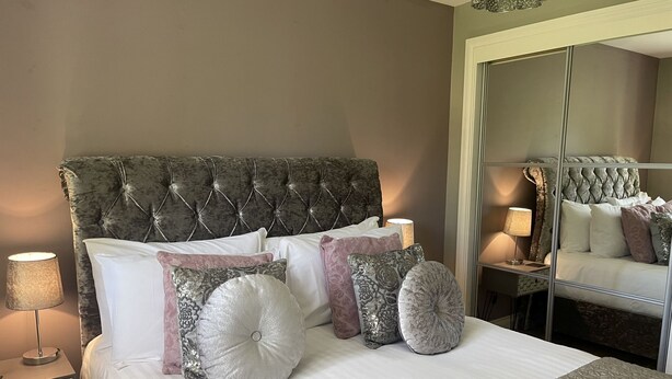 A neatly made bed with a tufted headboard, multiple pillows, and a bedside lamp.