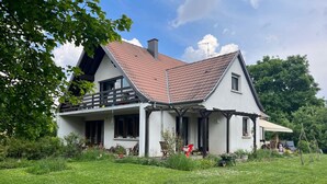 A two-story house with a red-tiled roof, a balcony, and a covered porch.